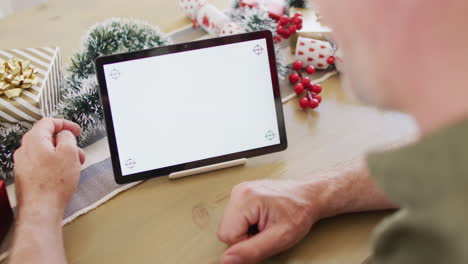 Happy-caucasian-man-wearing-santa-claus-hat,-using-tablet-with-copyspace-in-kitchen