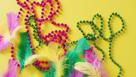 Video-of-pink-and-green-mardi-gras-carnival-beads-and-feathers-on-yellow-background-with-copy-space