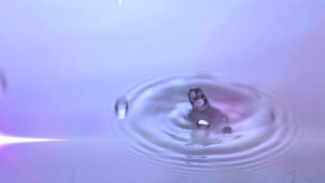 Animation-Von-Wassertropfen,-Die-Mit-Leuchtendem-Licht-In-Violettes-Wasser-Fallen