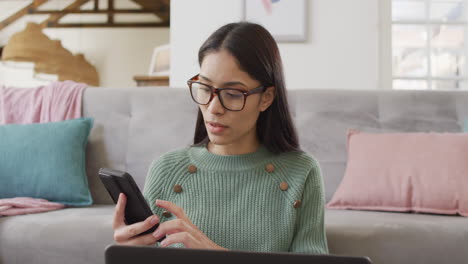 Biracial-woman-using-smartphone-and-working-in-living-room