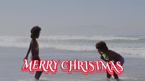 Animation-Von-„Frohe-Weihnachten“-über-Glückliche-Afroamerikanische-Kinder,-Die-Am-Strand-Spielen