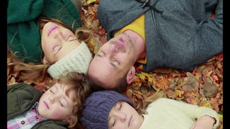 Family-lying-on-autumn-leaves-in-park