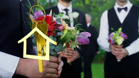 Animation-of-golden-house-keys-over-midsection-of-bridegroom-and-groomsman-holding-bouquet