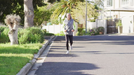 Video-of-senior-biracial-man-in-sports-clothes-and-headphones-running-on-sunny-street