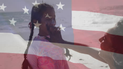 Animation-of-flag-of-united-states-of-america-over-biracial-mother-with-daughter-on-beach