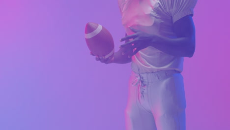 Video-of-midsection-of-african-american-american-football-player-with-ball-over-purple-background