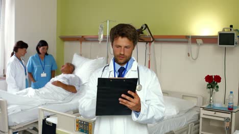 Der-Arzt-Liest-Den-Bericht,-Während-Die-Krankenschwester-Im-Hintergrund-Mit-Dem-Patienten-Interagiert