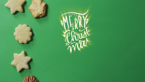 Animation-of-merry-christmas-over-cookies-on-green-surface