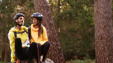 Mountain-biking-couple-sitting-on-a-rock-in-the-forest