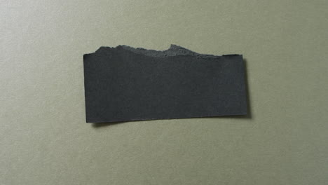 Video-of-close-up-of-torn-piece-of-black-paper-on-green-background