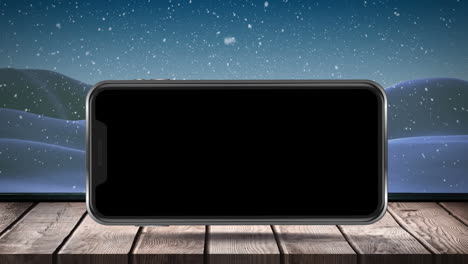 Animation-of-blank-smartphone-screen-with-winter-scenery-and-snow-falling-on-wooden-surface