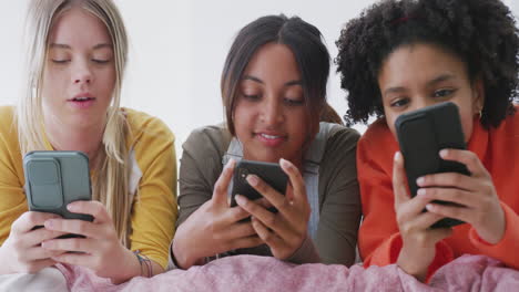 Fröhliche,-Vielfältige-Teenager-Freundinnen,-Die-Auf-Dem-Bett-Liegen-Und-Smartphones-Benutzen,-Zeitlupe