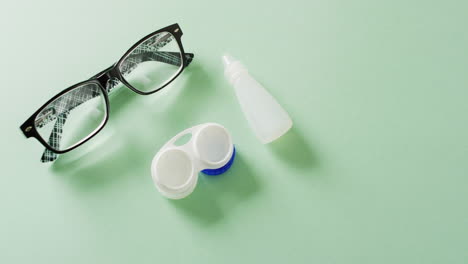 Video-of-glasses,-contact-lenses-case-and-lens-solution-on-green-background-with-copy-space
