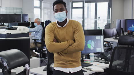 Man-wearing-face-mask-crossing-his-arms-while-standing-in-office