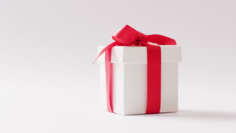 Video-of-side-view-of-white-gift-box-tied-with-red-ribbon,-on-white-background-with-copy-space