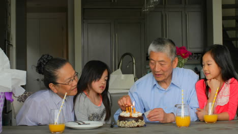 Front-view-of-old-senior-asian-grandfather-lightning-birthday-cake-candles-in-a-comfortable-home-4k