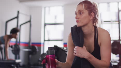 Video-of-caucasian-woman-drinking-water-taking-break-from-exercising-in-gym