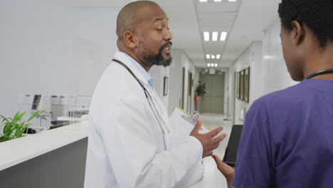 Médicos-Afroamericanos,-Hombres-Y-Mujeres,-Sosteniendo-Portapapeles-Y-Tableta,-Hablando-En-El-Hospital