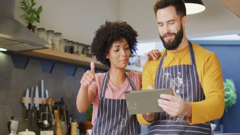 Video-of-happy-diverse-couple-in-aprons-using-tablet,-baking-together-in-kitchen,-with-copy-space
