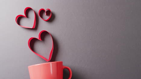 Video-of-red-mug-and-floating-red-heart-shapes,-on-grey-background-with-copy-space