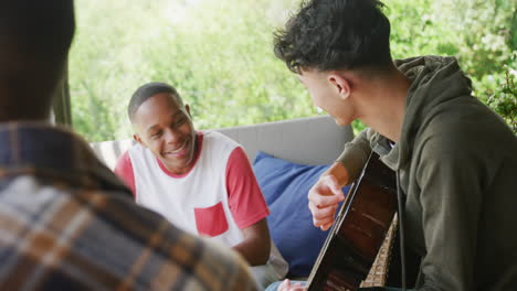 Happy-diverse-male-teenage-friends-playing-guitar-at-home,-slow-motion