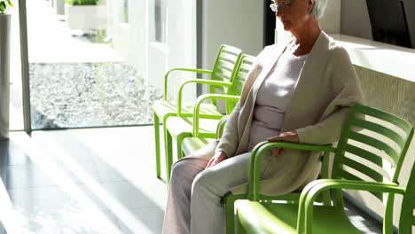 Thoughtful-senior-woman-sitting-on-chair-in-lobby