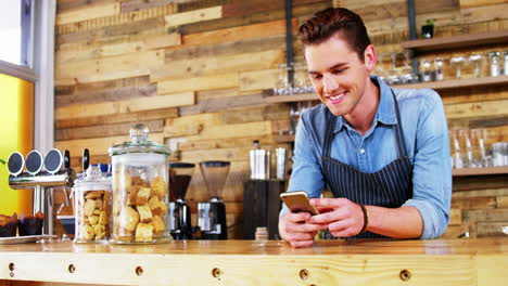 Male-waiter-using-mobile-phone-at-counter