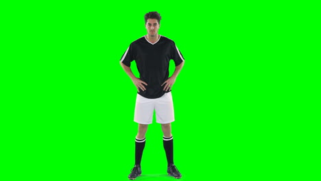 Confident-football-player-standing-against-green-screen