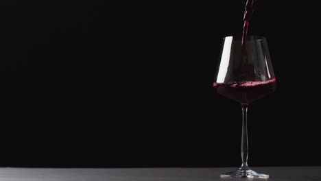 Rotwein,-Der-In-Glas-Auf-Schwarzem-Hintergrund-Mit-Kopierraum-Gegossen-Wird