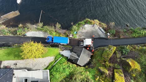 Truck-filling-asphalt-machine-with-more-asphalt-on-Norway-countryside-road-near-the-sea---High-angle-view-looking-down