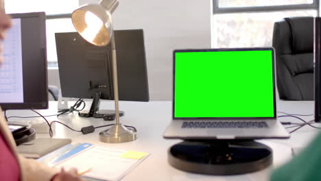 Opened-laptop-with-green-screen-on-desk-in-office