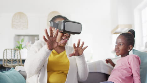 Excited-african-american-grandmother-using-vr-headset-sitting-with-granddaughter-at-home,-copy-space