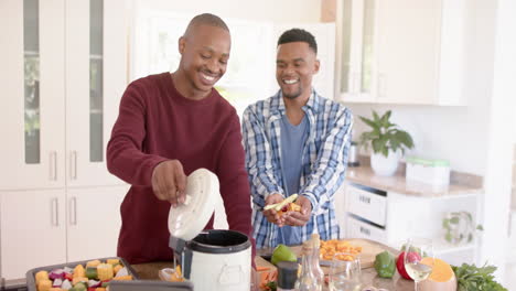 Glückliches-Afroamerikanisches-Schwules-Männliches-Paar,-Das-Das-Abendessen-Zubereitet,-Abfälle-In-Der-Küche-Reinigt,-Zeitlupe