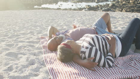Happy-senior-african-american-couple-lying-on-blanket-at-beach,-slow-motion