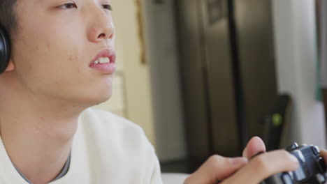 Nahaufnahme-Eines-Asiatischen-Jungen-Mit-Kopfhörern,-Der-Zu-Hause-Auf-Der-Couch-Videospiele-Spielt
