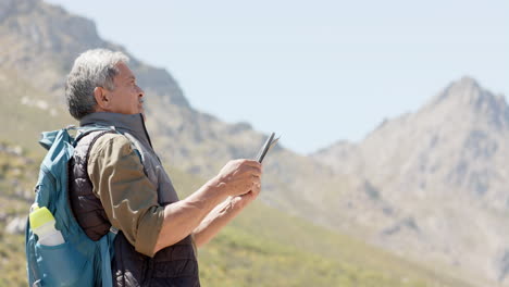 Senior-biracial-man-in-mountains-using-tablet,-in-slow-motion
