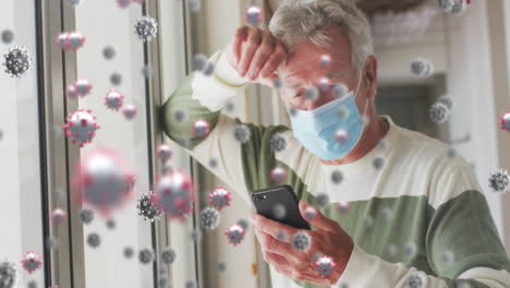 Animation-of-covid-cells-over-senior-man-and-woman-in-face-mask-using-smartphone