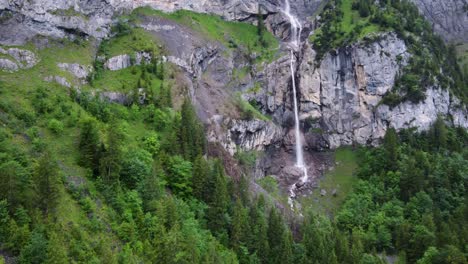 Almenbachfall-waterfall-flowing-among-pine-trees-and-alpine-rocks-in-Kandersteg-Switzerland,-Aerial