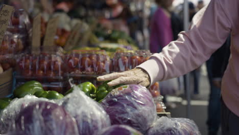 Slow-motion-shot-of-an-elderly-hand-touching-fresh-fruit-and-vegetables-on-offer-at-a-market