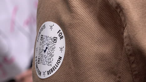 A-person-wears-a-white-sticker-on-their-jacket-sleeve-that-reads,-“Scientists-for-Extinction-Rebellion”-during-the-Restore-Nature-Now-protest