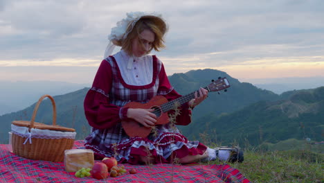 young-blonde-female-model-in-old-fashioned-traditional-clothing-having-lunch-alone-in-mountains-landscape-while-playing-string-guitar-instrument-historical-reproduction