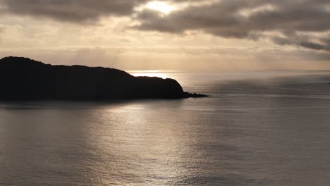 Goldener-Sonnenuntergang-über-Ruhigem-Wasser:-Die-Silhouette-Einer-Isolierten-Insel,-Getaucht-In-ätherisches-Licht