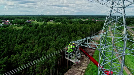 Aerial-view-of-electricians-on-a-power-pole-on-an-aerial-work-platform-or-cherry-picker-while-they-repair-the-power-lines-for-running-current-and-perform-dangerous-work-with-view-of-the-forest