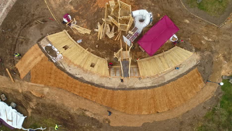Rising-and-spinning-aerial-birdseye-view-of-a-construction-site-with-construction-workers-as-they-build-a-wooden-building-on-a-productive-workday-on-the-construction-site
