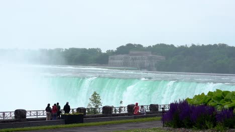 Static-wide-shot-of-the-beautiful-niagara-falls-in-the-canadian-province-of-ontario-with-view-of-the-huge-waterfall-and-pedestrians-or-tourists-on-the-railing-of-the-sight-in-slow-motion
