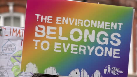 In-slow-motion-a-colourful-rainbow-Keep-Britain-Tidy-placard-is-held-up-that-reads,-“The-environment-belongs-to-everyone”-during-the-Restore-Nature-Now-protest