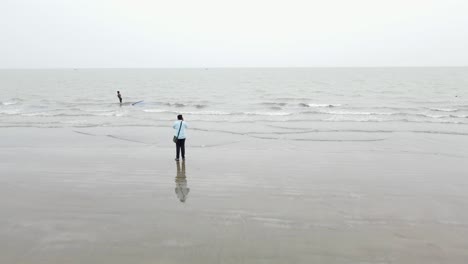 photographer-taking-picture-of-a-traditional-fisherman-pulling-his-net-at-the-Kuakata-Sea-Beach-in-Bangladesh,-Asia,-Drone