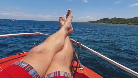 POV:-Hairy-male-legs-in-bow-of-red-boat-on-dark-blue-water-near-shore