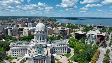 Aerial-view-of-Madison,-showcasing-the-stunning-Capitol-building-amidst-the-cityscape,-with-the-serene-backdrop-of-lakes-and-greenery