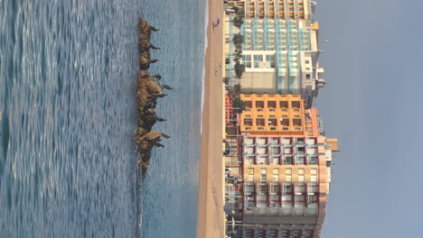 Vertical-video-of-the-Mediterranean-Sea-with-a-rock-with-cormorants-in-the-foreground-and-buildings-in-the-background-with-copy-space